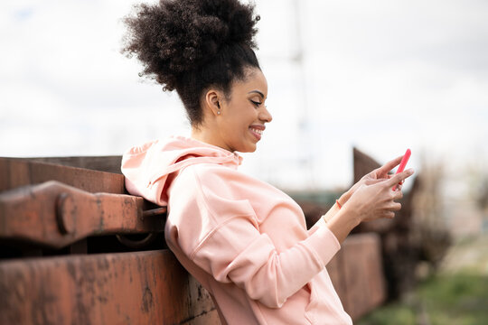 Smiling woman using smart phone while leaning on abandoned train in shunting yard