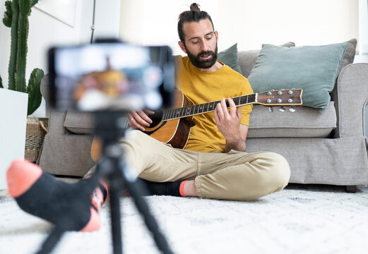 Male influencer vlogging while playing guitar at home