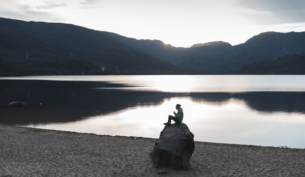 Man sitting on rock near lake during sunset