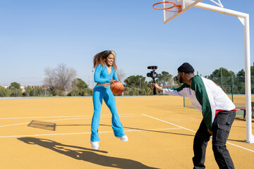 Happy male and female vlogging with basketball on sports court
