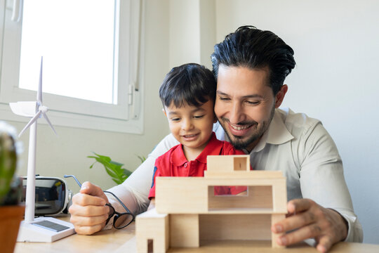 Male architect and son smiling while looking at house model