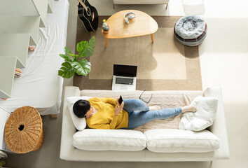 Relaxed woman using smart phone while lying on sofa in living room
