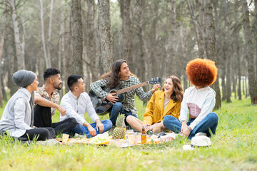 Young male and female friends playing guitar during picnic at forest