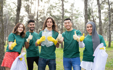 Young volunteer team gesturing thumbs up while holding plastic bottle in forest