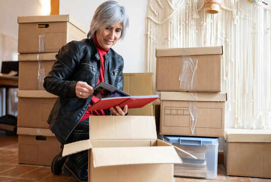 Mature woman in leather jacket watching photo album while kneeling at home