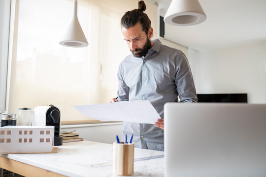 Handsome male architect looking at construction plan at home