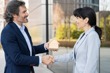 Smiling businesswoman doing handshake with real estate developer holding house model