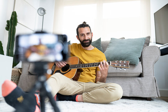 Smiling man vlogging while sitting with guitar at home