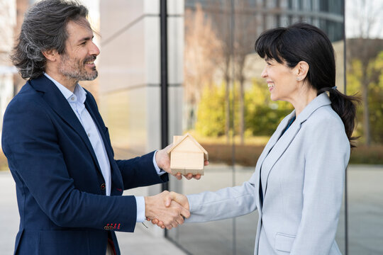 Smiling businesswoman doing handshake with real estate developer holding house model