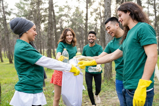Multi-ethnic volunteers collecting garbage in plastic bag at forest