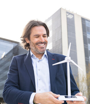 Happy male engineer looking at wind turbine model in city