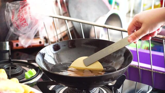 slow motion shot of fryum far far starchy bobby potato starch snack being put into boiling oil in a deep fryer where it expands puffs of steam come out and it's picked up with a sieve with the oil