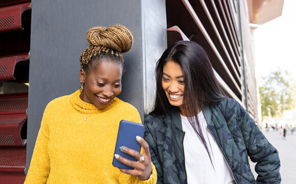 Multi-ethnic Female Friends Looking At Smart Phone By Wall