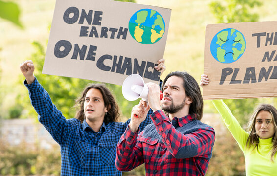 Long haired man holding megaphone while protesting with male and female protestors against climate change