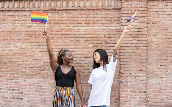 Lesbian couple waving rainbow flag by wall