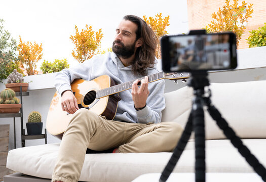 Male influencer vlogging while playing guitar on balcony