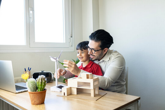 Male architect explaining wind turbine model to son at home