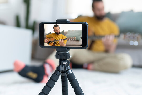 Handsome man filming while playing guitar at home