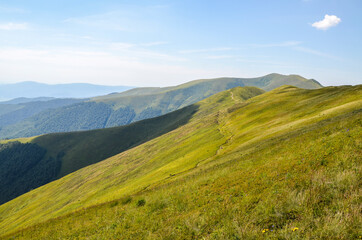 Carpathian summer landscape. Hiking path through grass field and mountain ridge with blue sky background. Ukraine