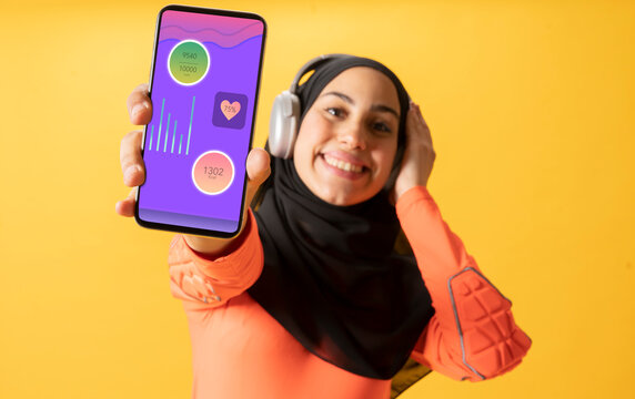 Smiling Arab woman showing an app on smart phone in front of yellow wall
