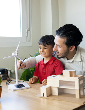 Smiling male architect discussing over wind turbine model with son at home