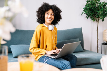 Contemplating young woman with laptop sitting on sofa at home