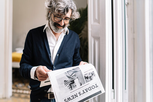 Senior man with in-ear headphones reading newspaper at home