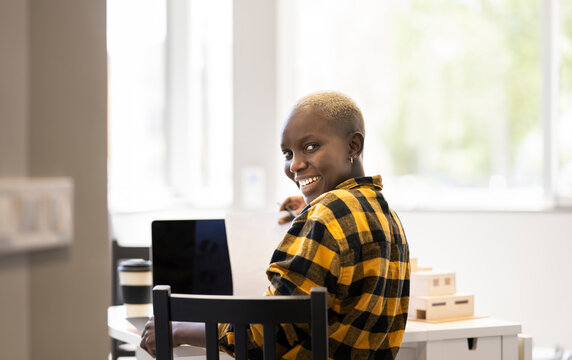 Smiling female architect looking over shoulder while working at home