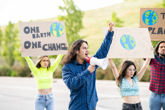 Male activist with megaphone announcing on climate change with protestors in background on footpath