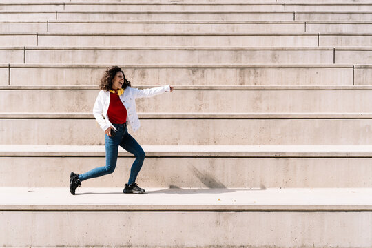Carefree woman with headphones dancing on staircase during sunny day