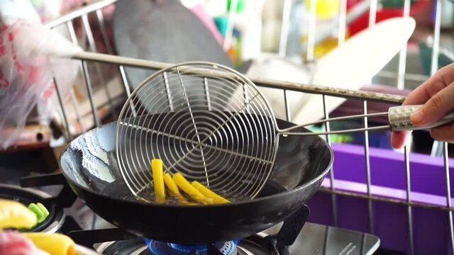 slow motion shot of fryum far far starchy bobby potato starch snack being put into boiling oil in a deep fryer where it expands puffs of steam come out and it's picked up with a sieve with the oil