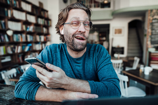 Male entrepreneur winking eye while holding smart phone in coffee shop