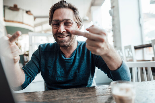Happy male entrepreneur showing obscene gesture at cafe