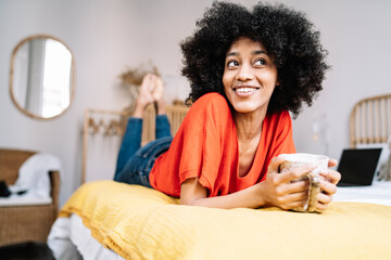Contemplating woman with mug lying on bed at home