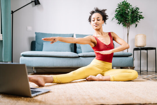Woman doing yoga while watching online tutorial on laptop at home