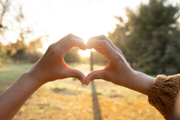 Hands of young woman making heart shape during sunset