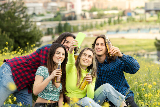 Woman taking selfie with male and female friends while having beer on field in nature