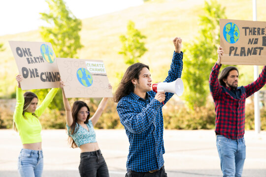 Young male activist protesting on climate change with male and female protestors on footpath