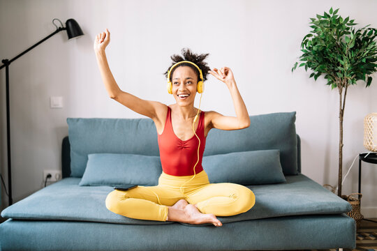 Young woman enjoying music over headphones sitting on sofa at home