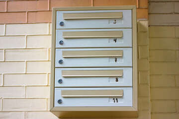 Gray-yellow multi-section metal mailbox against the beige brick wall. Apartment numbers 3, 4, 7, 8, 11. Boxes for newspapers, correspondence, letters in the entrance hall of an apartment building.