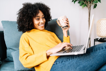 Young woman using laptop while holding mug at home
