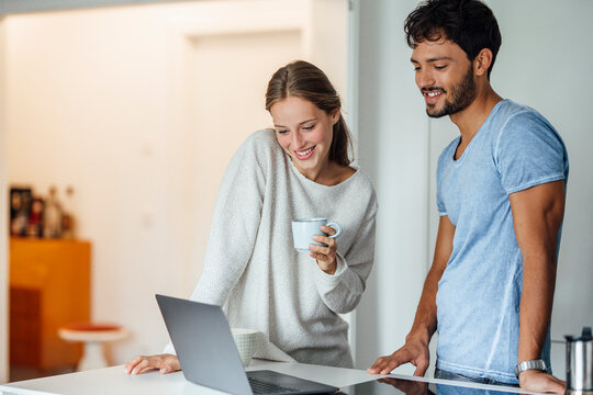 Happy woman looking at laptop while standing by boyfriend at home