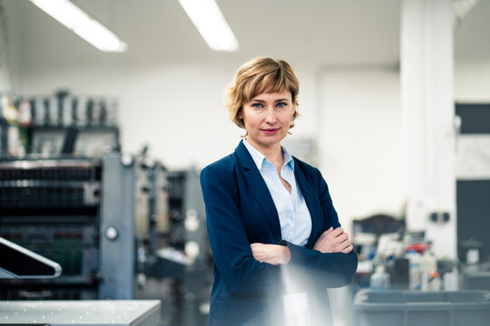 Confident businesswoman standing with arms crossed in printing factory