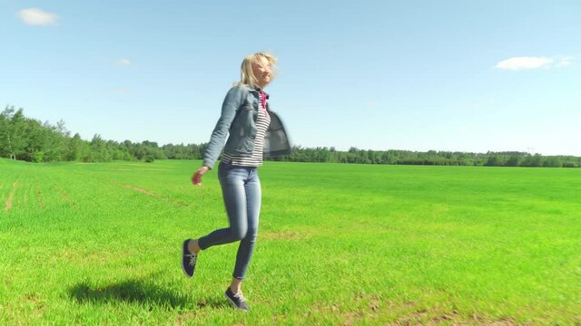 Woman dancing feel happy in the landscape grass field meadow nature summer in the sun hair young spring model pretty relax happiness. She's wearing a denim suit, and jeans.