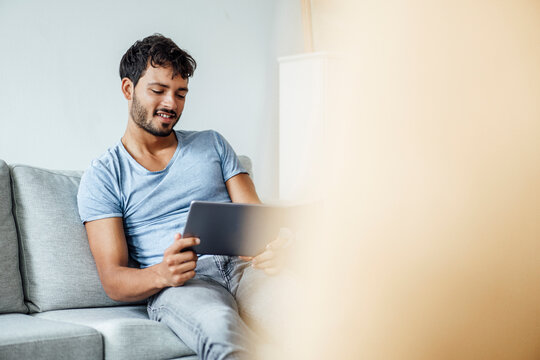 Smiling young man using digital tablet while sitting on sofa at home