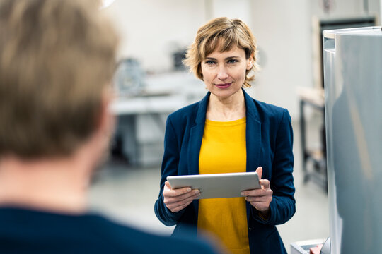 Mature manager holding digital tablet while standing with colleague in workshop