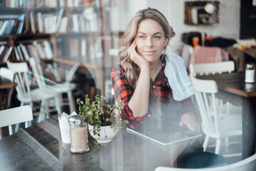 Female waitress with hand on chin contemplating by window at cafe