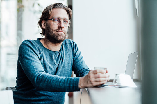 Thoughtful man by laptop in coffee shop during pandemic