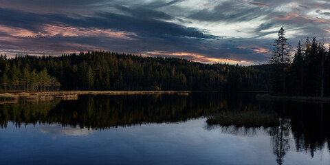 Fototapeta na wymiar Sunrise over the lake. The sky is dramatic and on fire. Shot in Nordmarka, Oslo, Norway. 