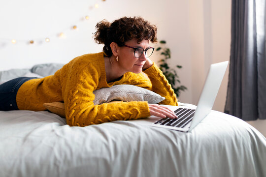 Mature Woman Using Laptop While Lying On Bed At Home